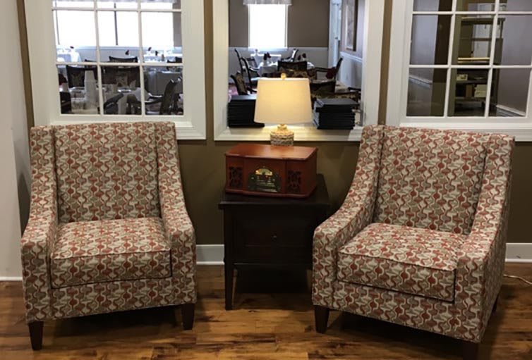 Two patterned chairs flank a small table with a lamp in a cozy living room setting.