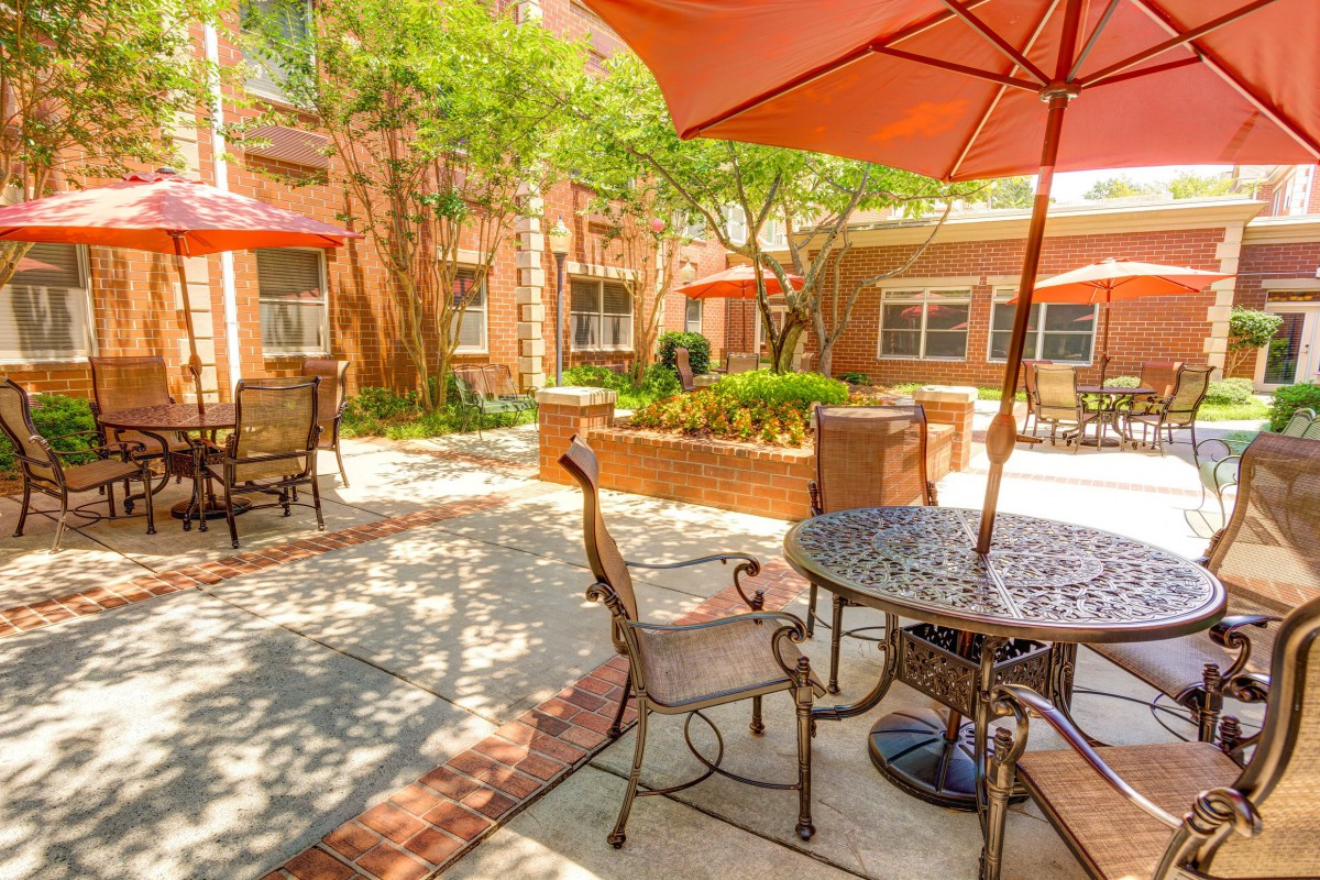 A sunny courtyard with patio furniture and umbrellas, surrounded by brick buildings.