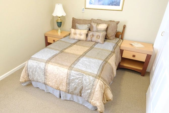 A cozy bedroom setup featuring a neatly made bed with patterned bedding, flanked by wooden nightstands and a stylish lamp.