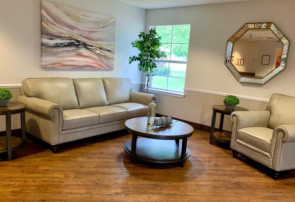 A cozy living room with a beige sofa set, round coffee table, wall art, indoor plant, and a decorative mirror.