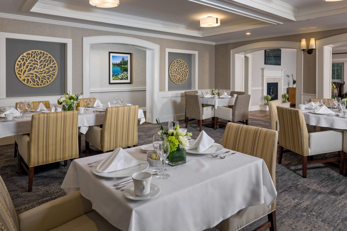 An elegantly designed dining room with neatly arranged tables and chairs, adorned with flowers and artwork.