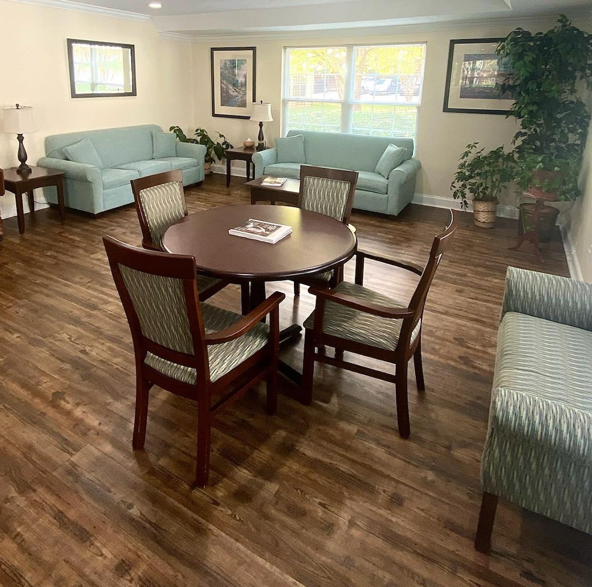 A cozy living room with a wooden floor, featuring sofas and a dining table with chairs.
