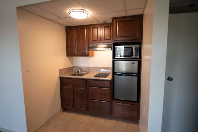 A compact kitchenette featuring wooden cabinets, a sink, and built-in appliances including an oven and microwave.