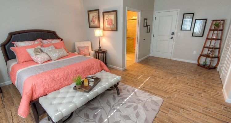 A cozy and stylish bedroom featuring a bed with coral bedding, a white tufted bench, and elegant wall art.