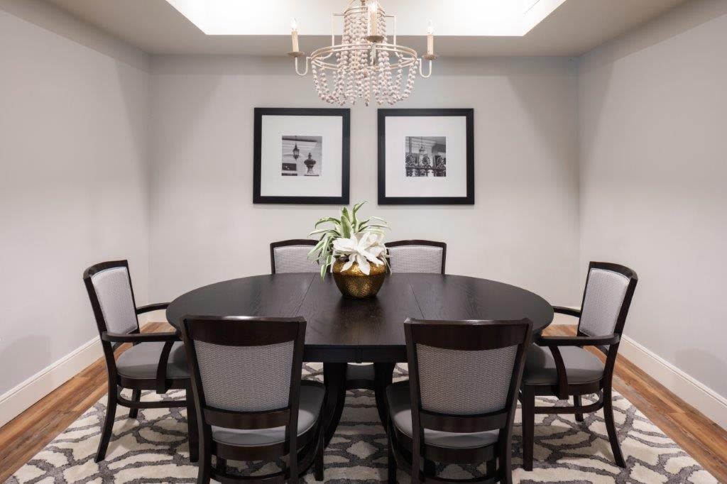 A cozy dining room featuring a round table with surrounding chairs, adorned by a chandelier and framed artwork.