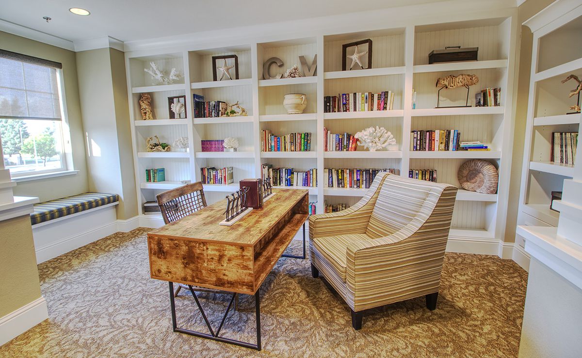 A cozy home office with a wooden desk and comfortable chair surrounded by bookshelves.