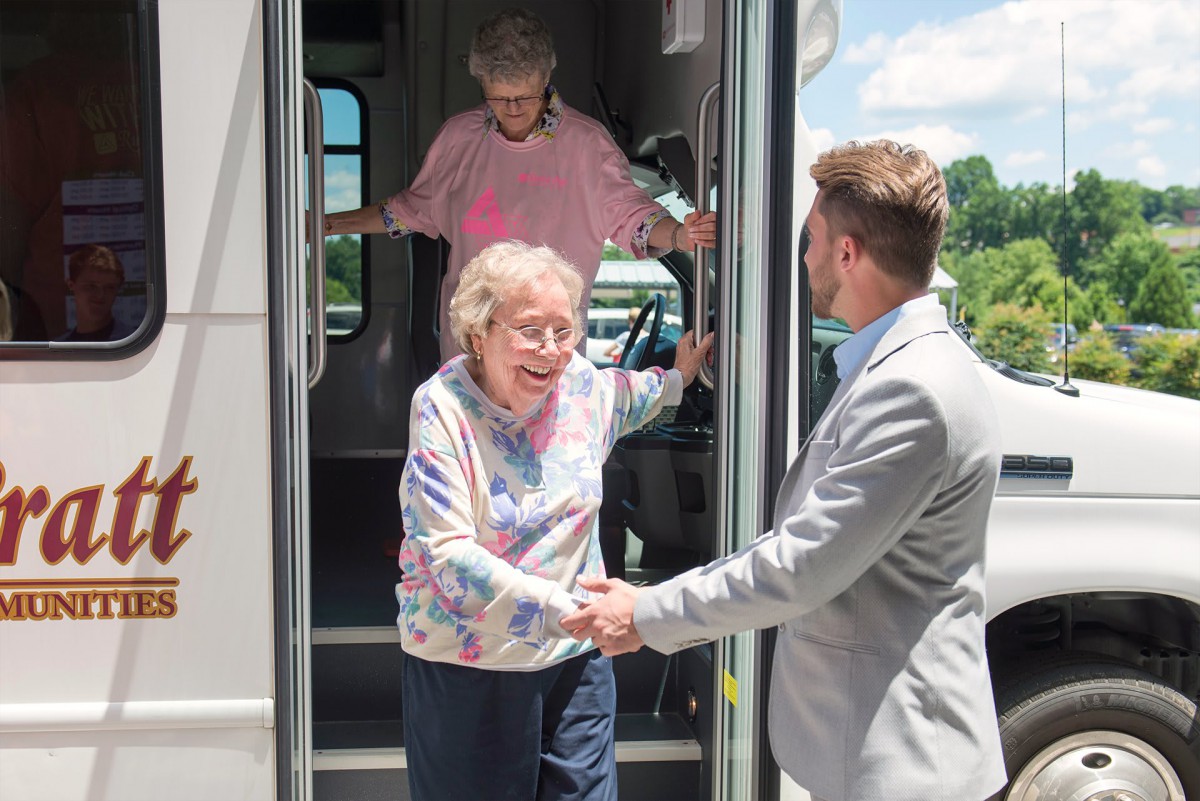 An elderly woman receives assistance while stepping off a bus.