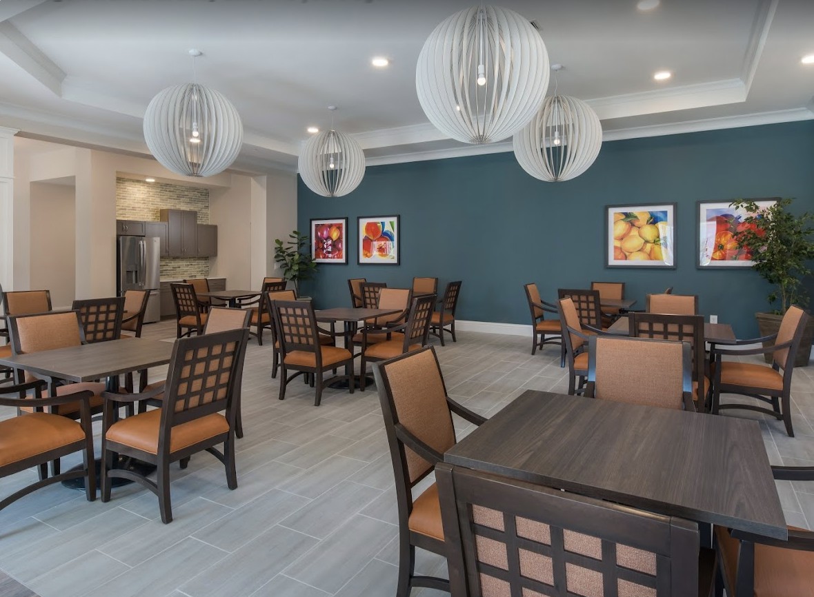 A modern dining area with neatly arranged tables and chairs, featuring stylish hanging lights and colorful artwork on the walls.
