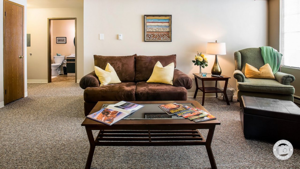 A cozy living room with a brown sofa, decorative pillows, and a wooden coffee table topped with magazines.