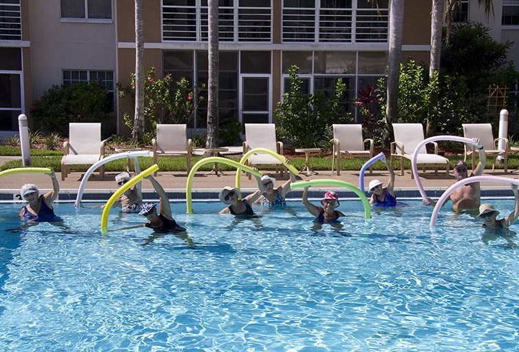 A group of people exercising with pool noodles in an outdoor swimming pool.