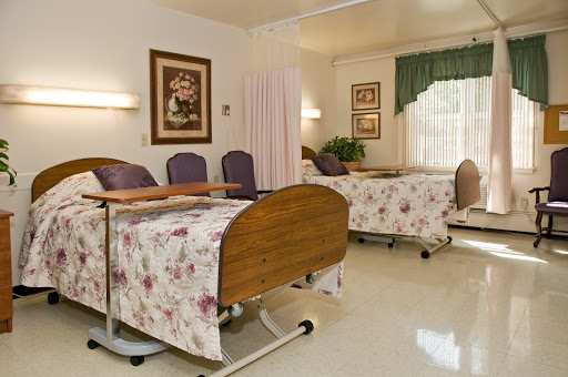 A well-maintained patient room in a medical facility, featuring floral-patterned bedding and comfortable seating.