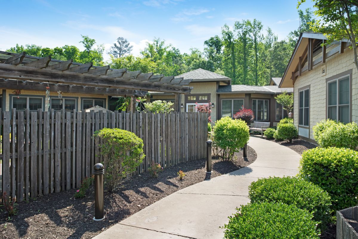 A peaceful garden setting with a winding pathway surrounded by manicured shrubs and a wooden fence.