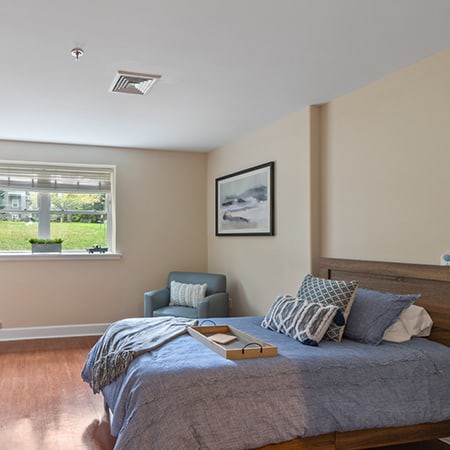 A modern bedroom with stylish decor, featuring a bed, chair, and large window.