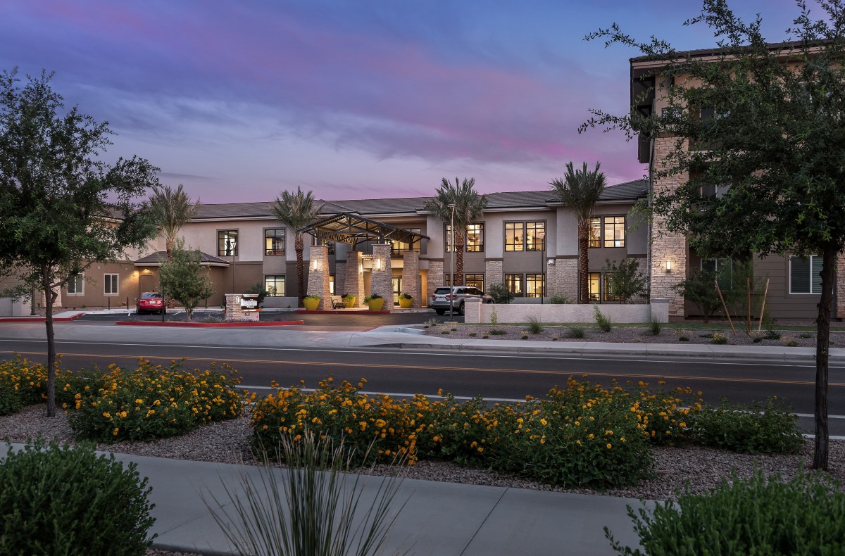 An illuminated building surrounded by landscaping at dusk, under a colorful sky.