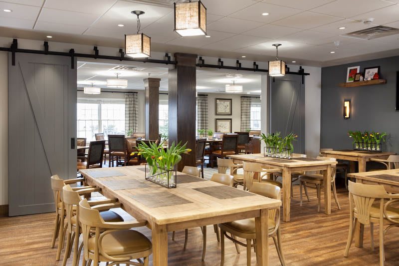 A modern dining area featuring wooden tables, chairs, and stylish lighting, complemented by greenery for a cozy atmosphere.