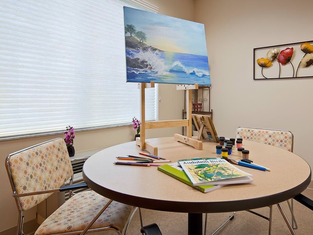 An art studio with a painting of an ocean scene on an easel, surrounded by art supplies on a round table.
