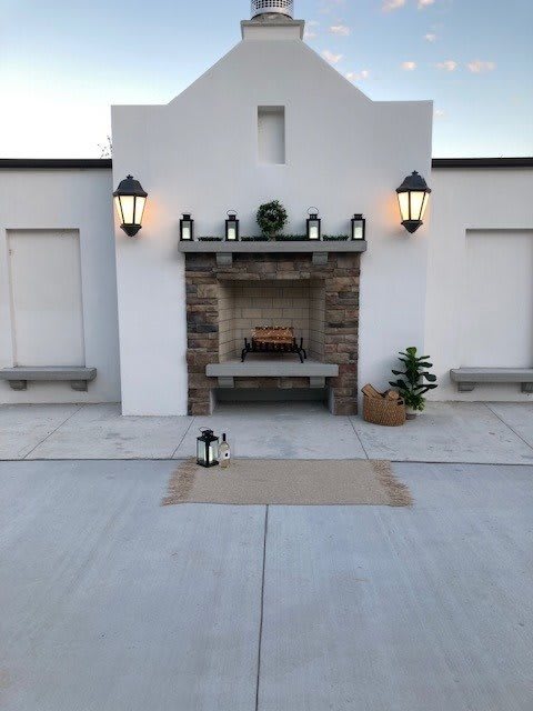 An elegant outdoor patio with a central fireplace, flanked by lanterns and simple decor.