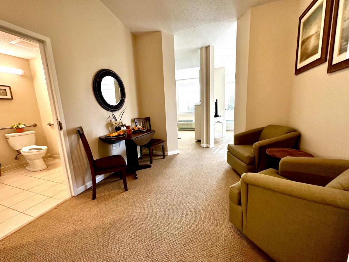 A cozy living area with chairs, a desk, and a mirror in a well-lit room.