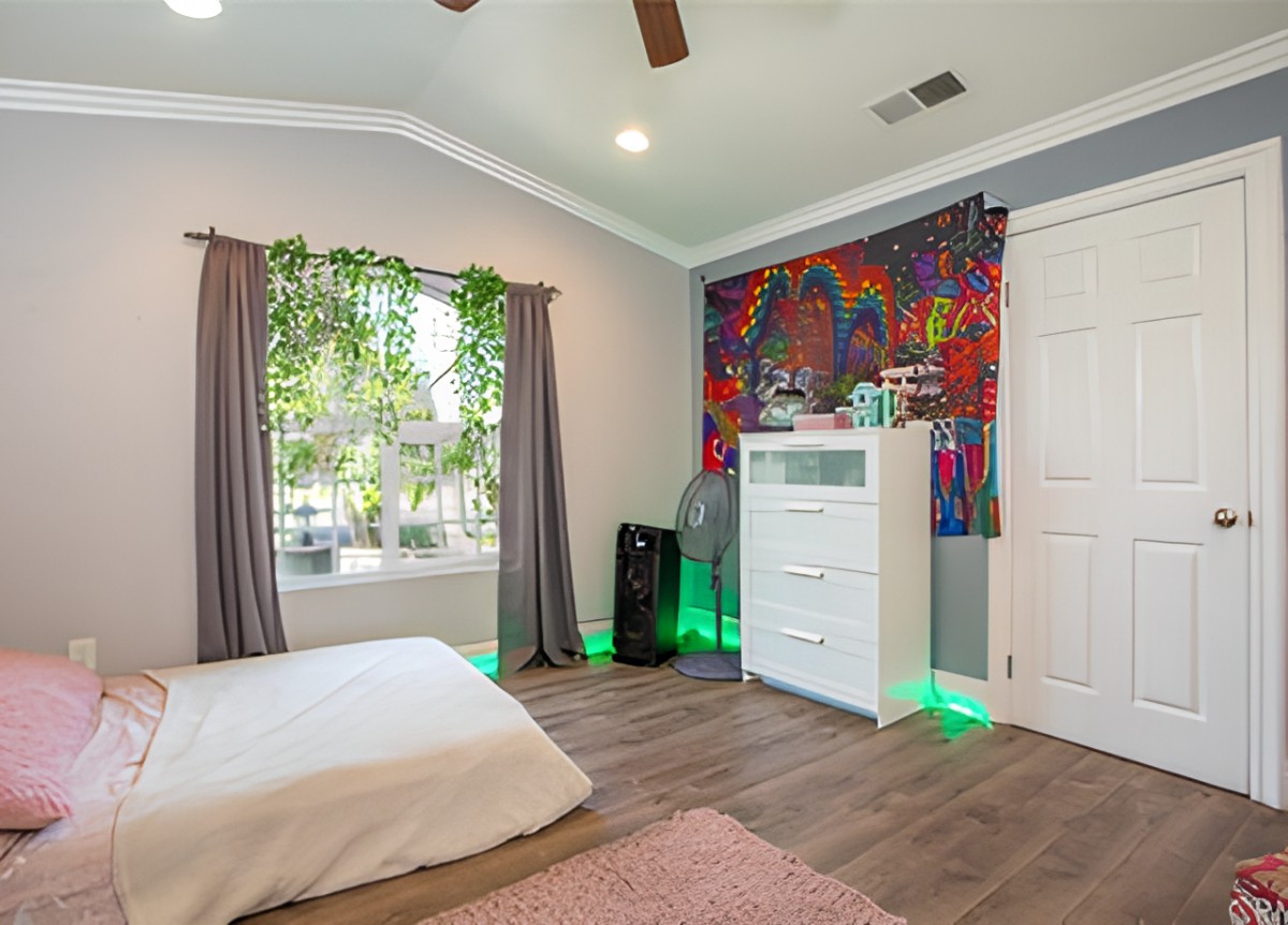 A cozy bedroom featuring a colorful mural, abundant natural light, and modern decor with plants and wood flooring.