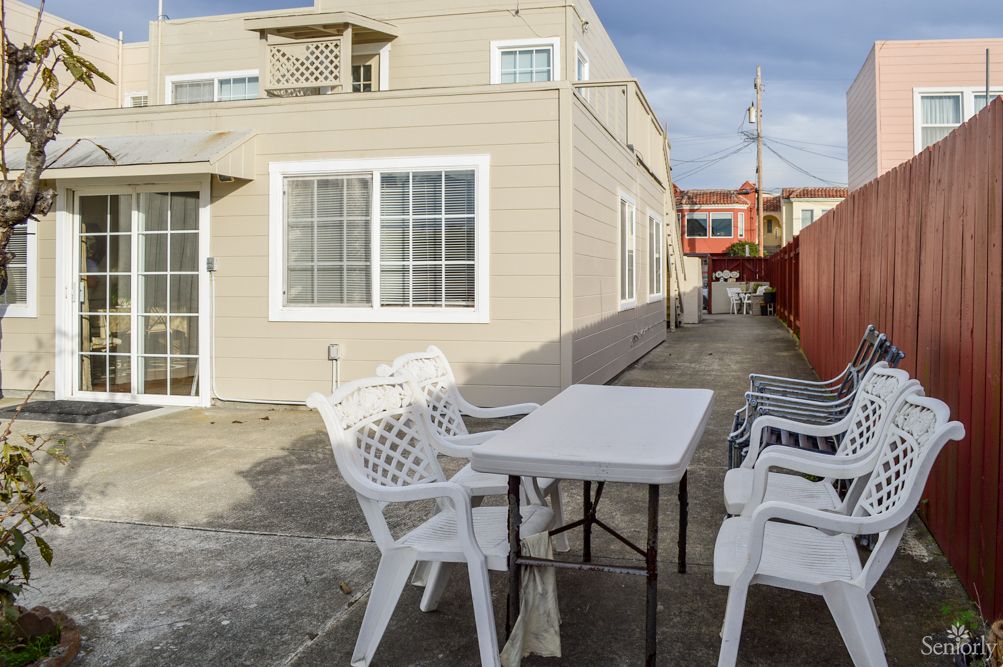 A patio area with white plastic chairs and a table next to a house.