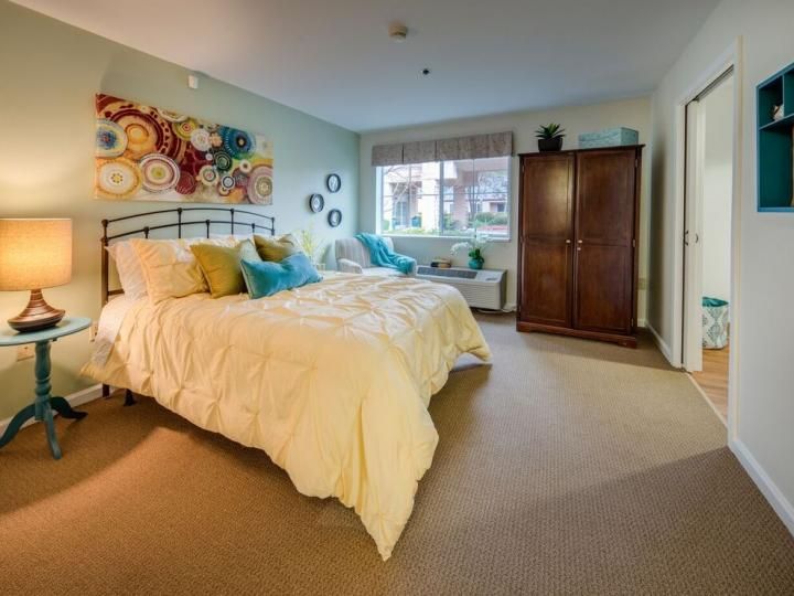 A cozy bedroom with a large bed, colorful pillows, abstract art on the wall, and a wooden wardrobe.