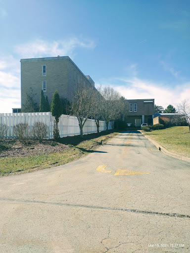 An abandoned building along a deserted road, surrounded by a fence and sparse vegetation.