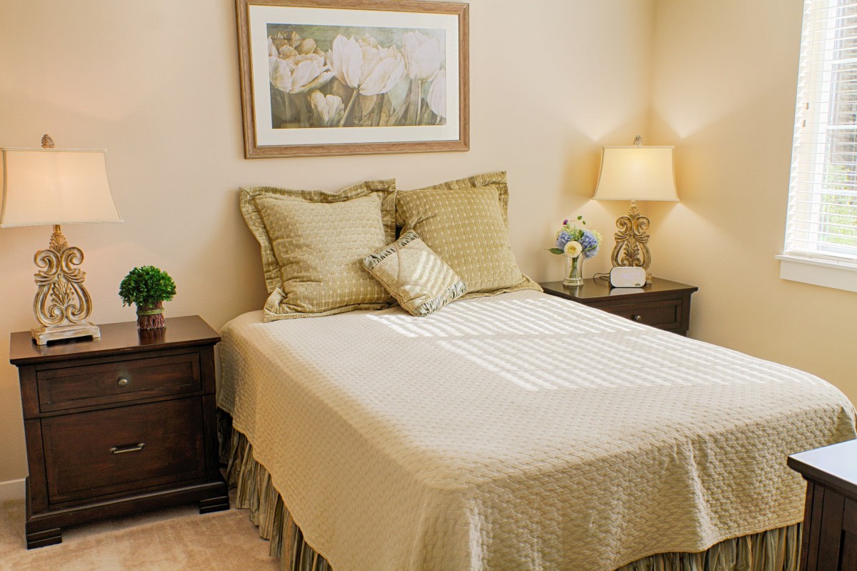 A cozy bedroom with a neatly made bed, decorative pillows, and matching nightstands with lamps.