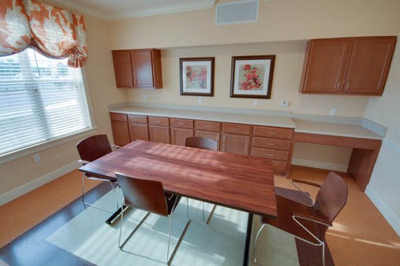 A light-filled dining room featuring a wooden table, chairs, cabinetry, and decorative artwork on the wall.