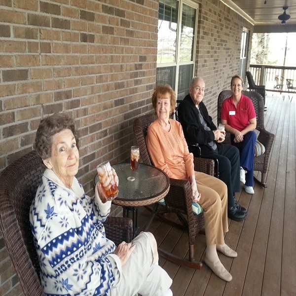 A group of elderly individuals sitting on a porch, enjoying drinks and relaxing together.