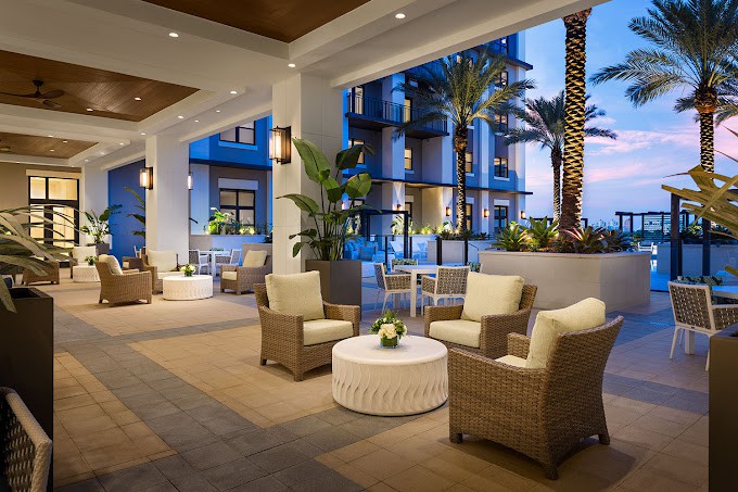 A luxurious outdoor lounge area at a resort featuring comfortable wicker seating and palm trees in the evening light.