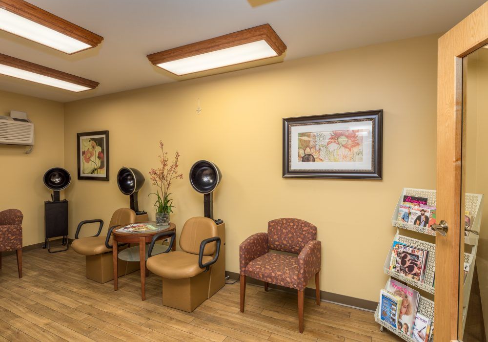 A cozy waiting room with chairs, brochures, and salon equipment against a warmly painted wall.