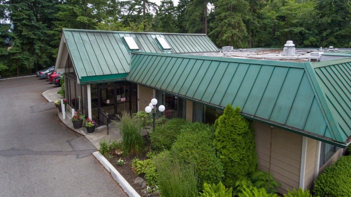 A building with a green metal roof surrounded by lush landscaping and trees.