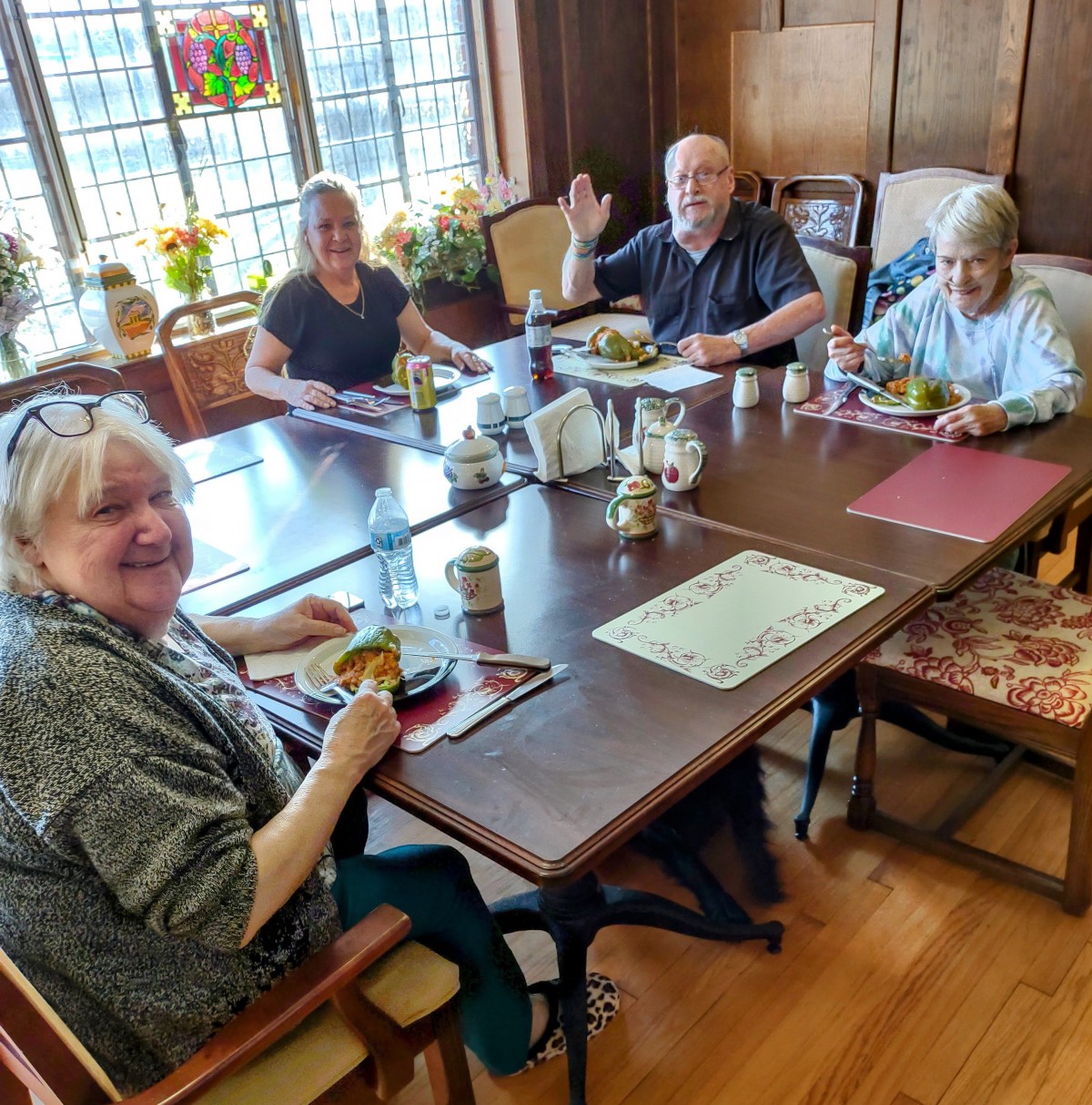 A group of people enjoying a meal together at a dining table inside a room with wooden walls and stained glass windows.