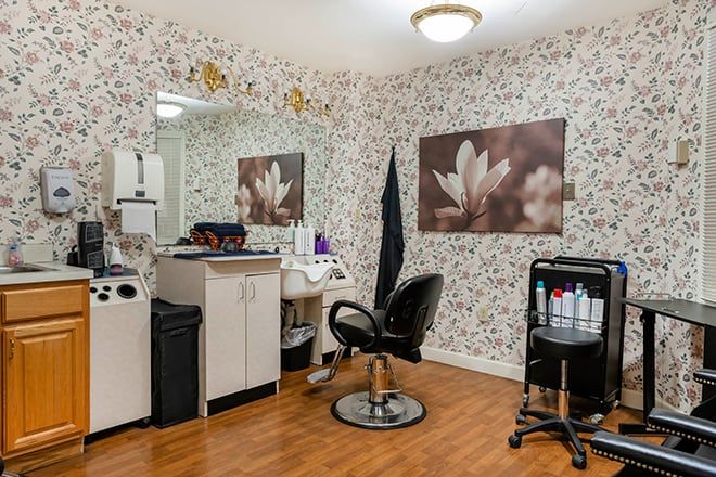 A cozy hair salon interior with floral wallpaper, a styling chair, and beauty products neatly arranged on the counter.