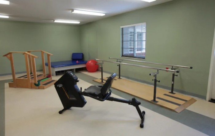 A rehabilitation room with exercise equipment, including parallel bars and a recumbent bike.