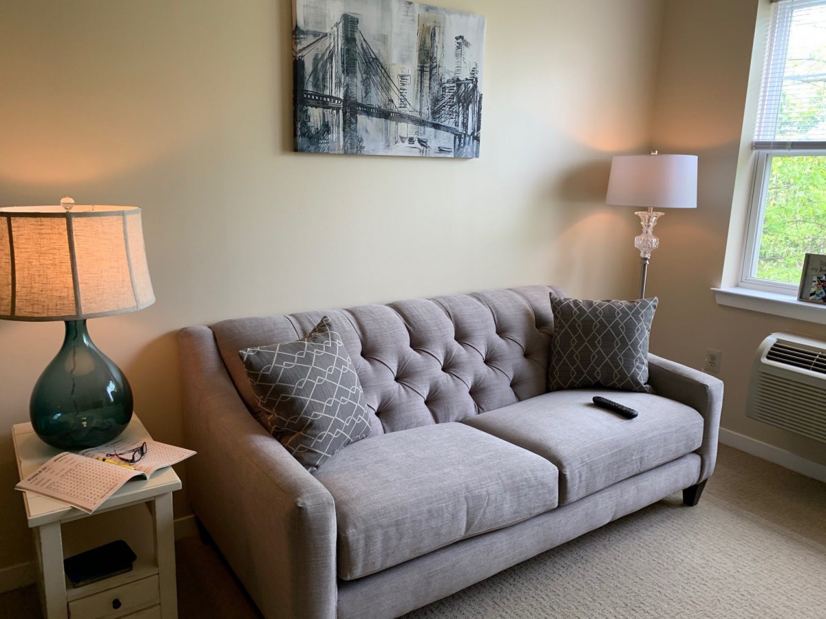 A cozy living room with a tufted sofa, decorated with patterned cushions, alongside matching lamps and wall art.