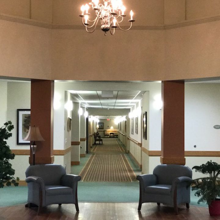 A well-lit hallway with two chairs under a chandelier.