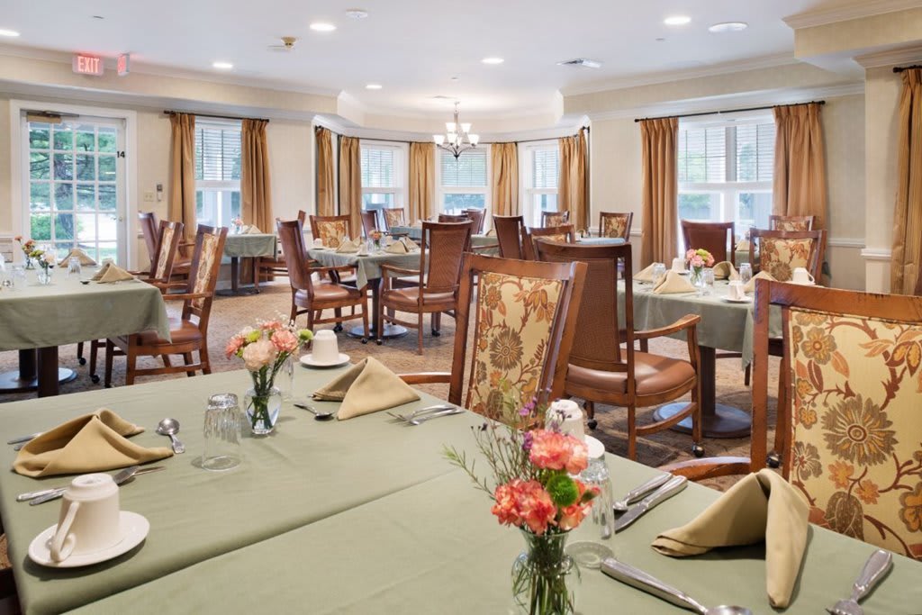 An elegant dining room with neatly arranged tables and chairs, decorated with flowers and napkins.