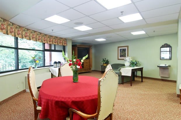 A well-lit dining area with a table covered by a red cloth and decorated with flowers.
