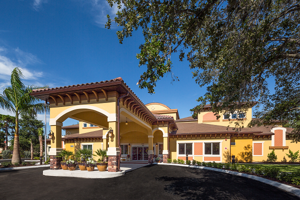 A sunny view of a building's entrance with Mediterranean-style architecture and surrounding landscaping.
