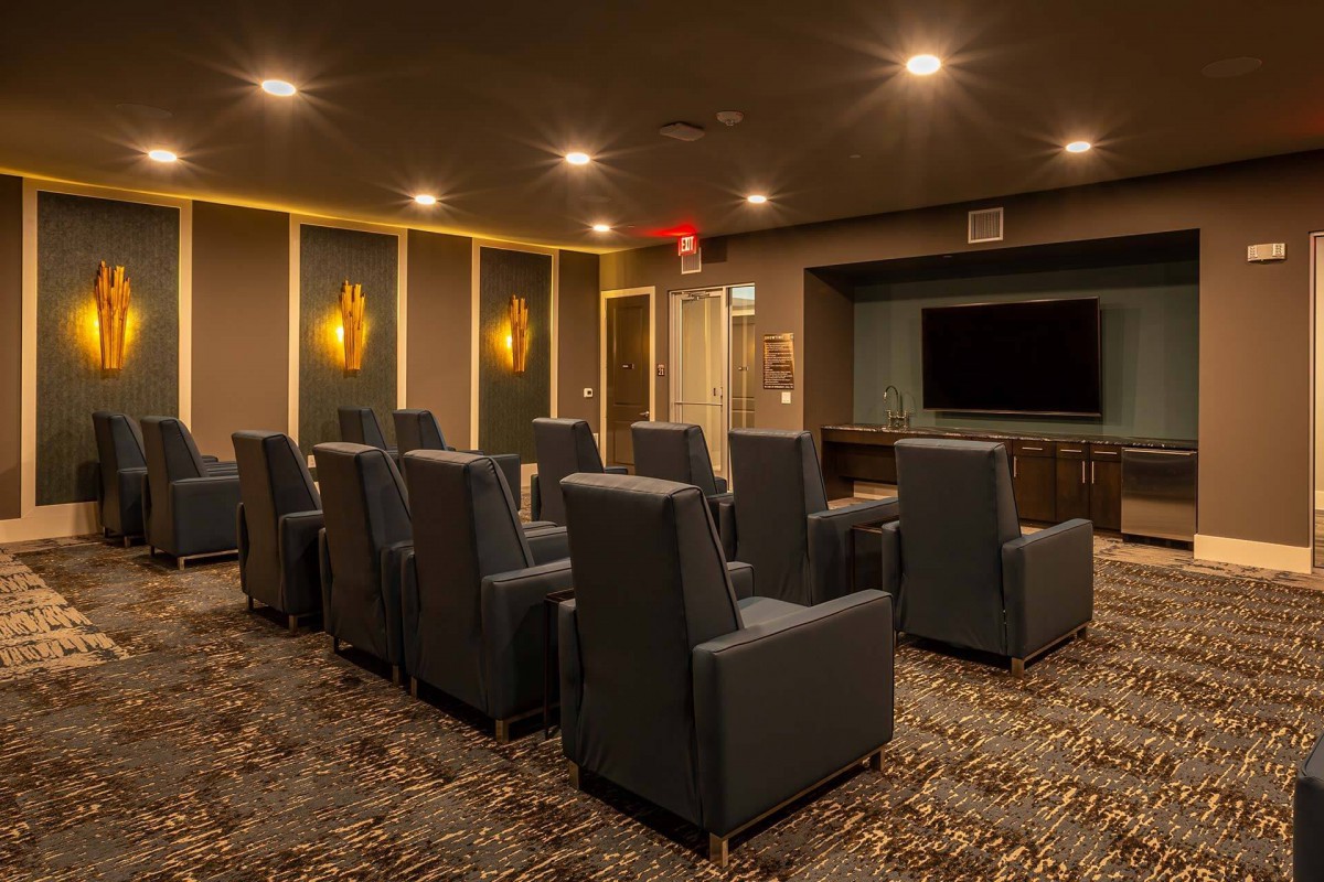 A cozy home theater room with multiple recliner chairs and a large screen, featuring warm lighting.