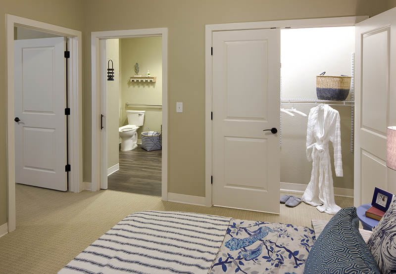 A cozy bedroom with a view of the bathroom and closet area, featuring neutral tones and striped bedding.