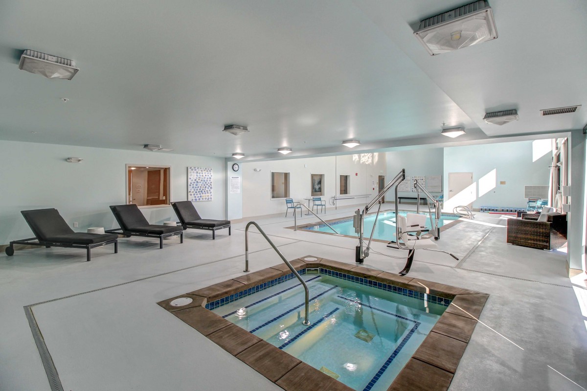 An indoor recreation area featuring a swimming pool and hot tub with lounge chairs nearby.