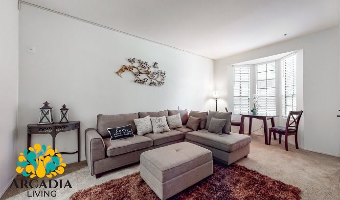 A cozy living room with a sectional sofa, ottoman, and decorative wall art.