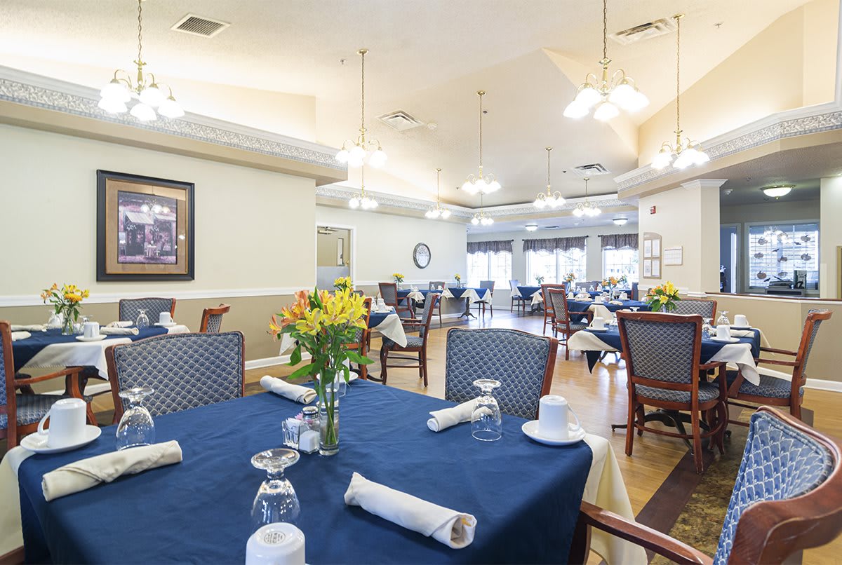 An elegant dining room setup with tables covered in blue tablecloths and decorated with floral centerpieces.