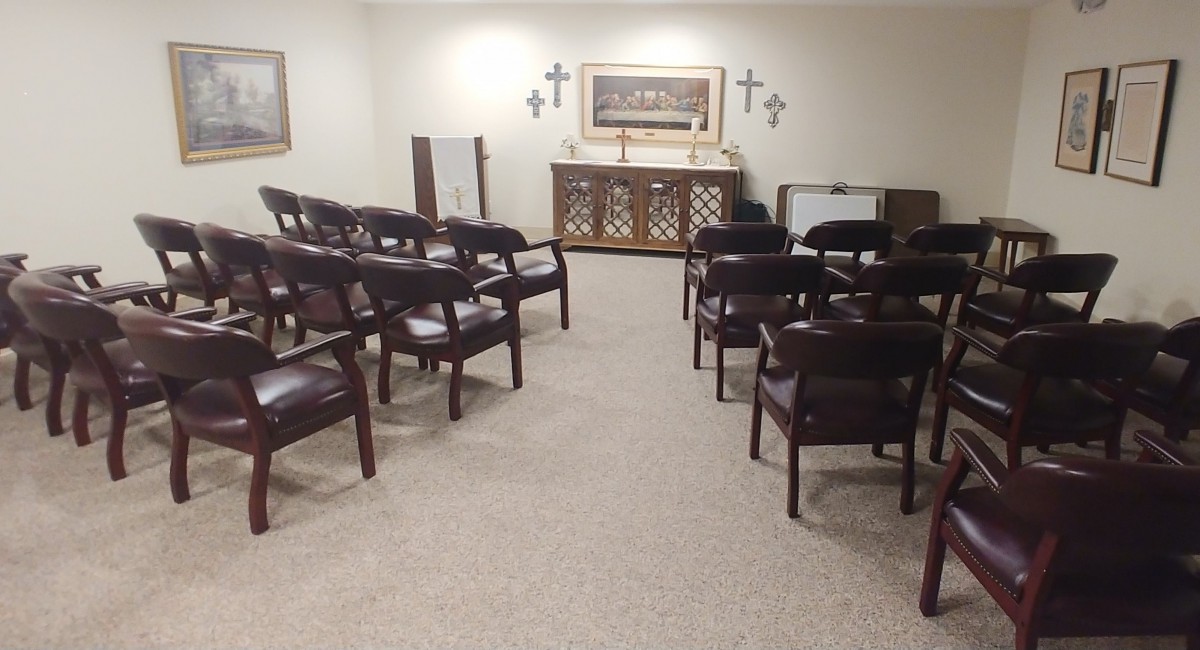 A small chapel with neatly arranged chairs facing an altar adorned with crosses.