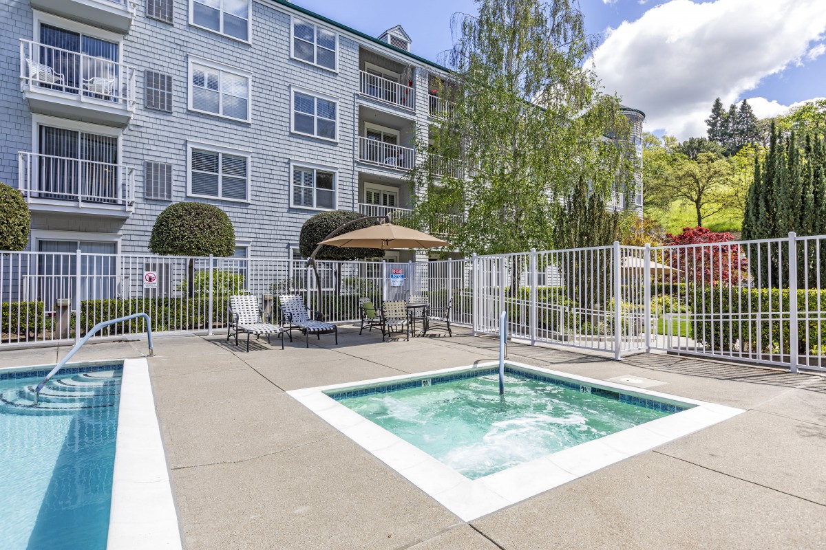 Outdoor swimming pool area with seating in front of an apartment building.