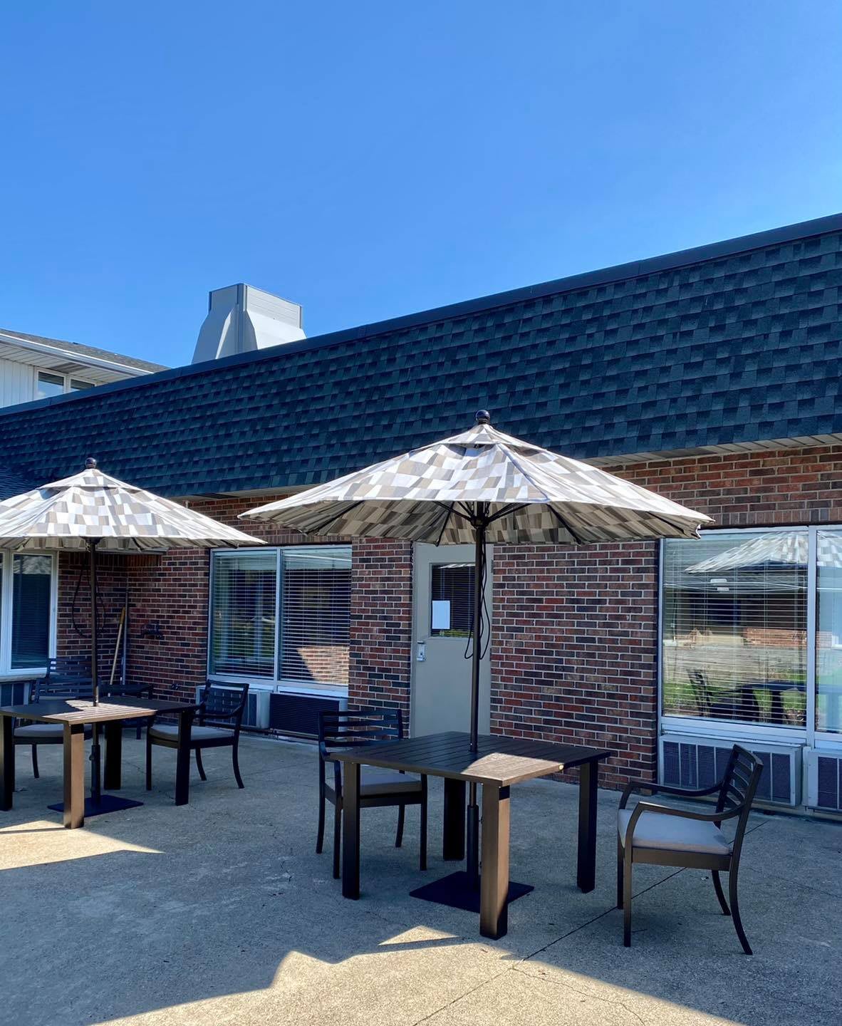 A cozy outdoor patio with tables and umbrellas against a brick building under a clear blue sky.