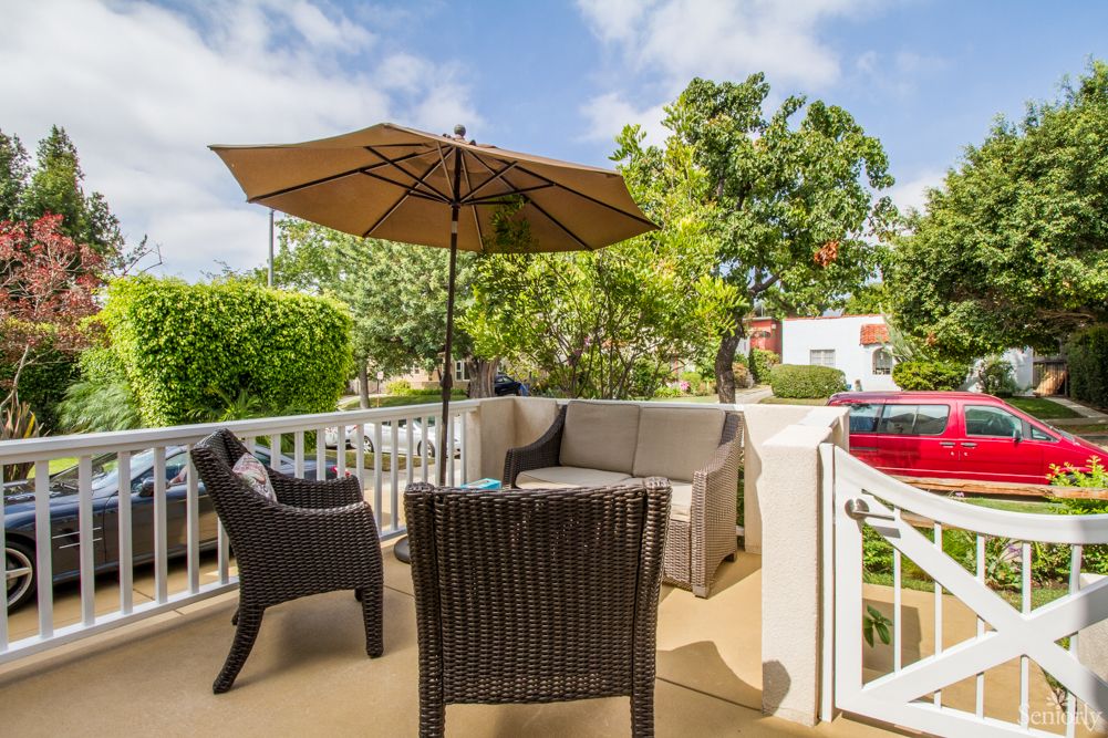 A cozy patio setup with wicker furniture and a sun umbrella, surrounded by greenery.