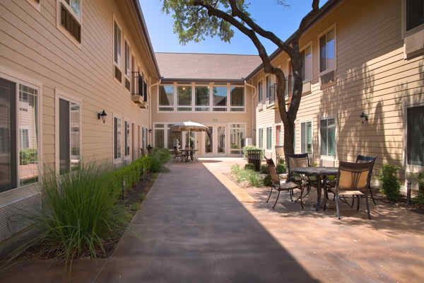 A peaceful courtyard with outdoor seating and a path lined by buildings under a clear blue sky.